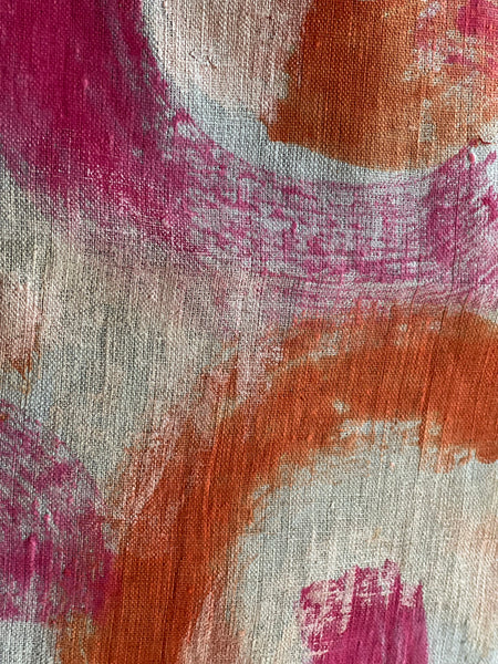 Abstract painted fabric closeup with broad brushstrokes in terracotta orange, magenta pink, and off-white with visible woven texture.