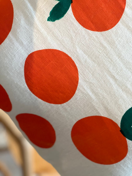A close-up of a white fabric with a bold pattern of large oranges and small dark green leaves.